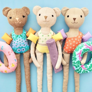 May include: Three handmade bear dolls wearing swimsuits and holding pool floats. The bears have different colored swimsuits and floats. The image also includes the text "BEAR BIKINI & SWIMSUIT" and "PDF PATTERN".
