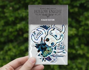May include: A package of stickers featuring characters from the video game Hollow Knight. The stickers are in a Kawaii Edition, with a variety of character designs in white, blue, and black. The package has a gray header with the game's name.