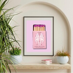 May include: Pink matchbox with a pink and white illustration of the Gemini zodiac sign. The text on the box reads "Gemini, Curious and Clever, May 21st - June 20th".