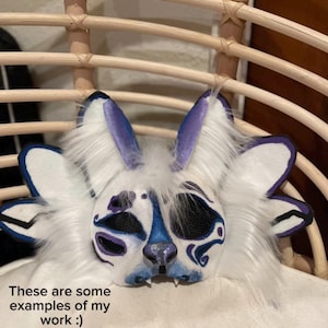 May include: A white and blue furry mask with purple accents, resembling a rabbit or similar creature. The mask has large ears and detailed facial features. Text on the image reads: "These are some examples of my work :)"