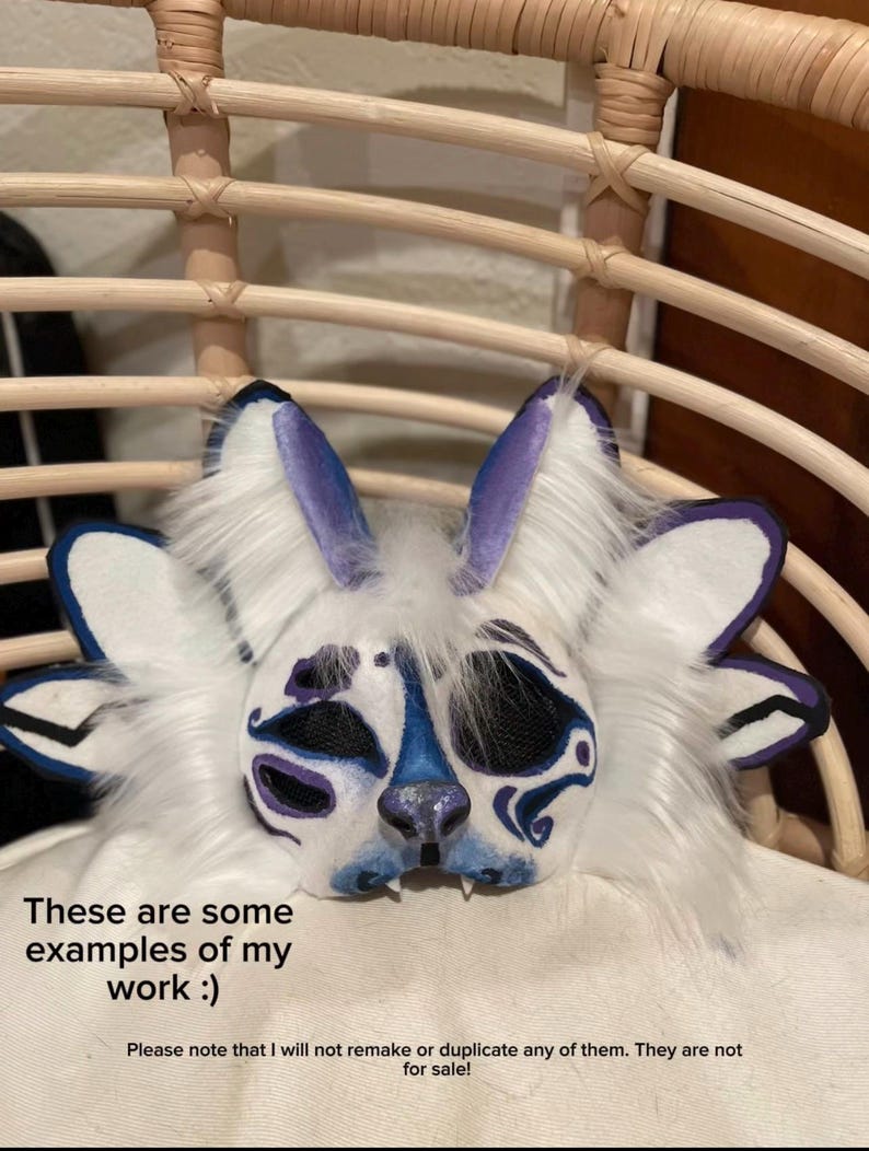 May include: A white and blue furry mask with purple accents, resembling a rabbit or similar creature. The mask has large ears and detailed facial features. Text on the image reads: "These are some examples of my work :)"