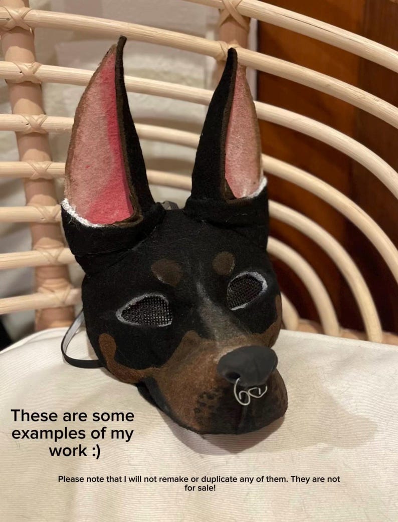 May include: A black and brown Doberman Pinscher mask with mesh eye coverings and a silver nose ring. The mask has pink inner ears and is displayed on a white surface. Text on the image reads "These are some examples of my work :)" and "Please note that I will not remake or duplicate any of them. They are not for sale!"