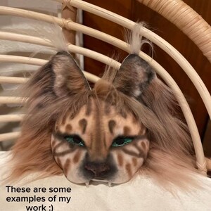 May include: A detailed, handmade mask with a feline design, featuring brown and tan fur, green eyes, and visible fangs. The mask is displayed on a white surface, with text at the bottom stating, "These are some examples of my work :)" and other text below.