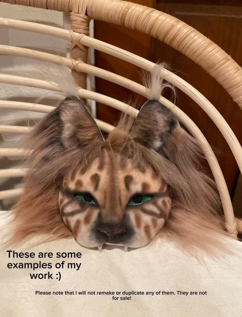 May include: A detailed, handmade mask with a feline design, featuring brown and tan fur, green eyes, and visible fangs. The mask is displayed on a white surface, with text at the bottom stating, "These are some examples of my work :)" and other text below.