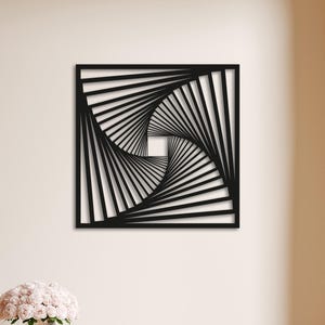 May include: Black square wall art with a geometric spiral design. The artwork is mounted on a beige wall above a light pink bench. The room has a neutral colour palette with a white door and hardwood flooring.
