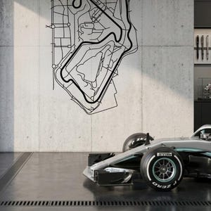 May include: A black and white Silverstone Circuit map is mounted on a concrete wall. The text "SILVERSTONE CIRCUIT" is above the map. A silver and black race car is parked in front of the wall.