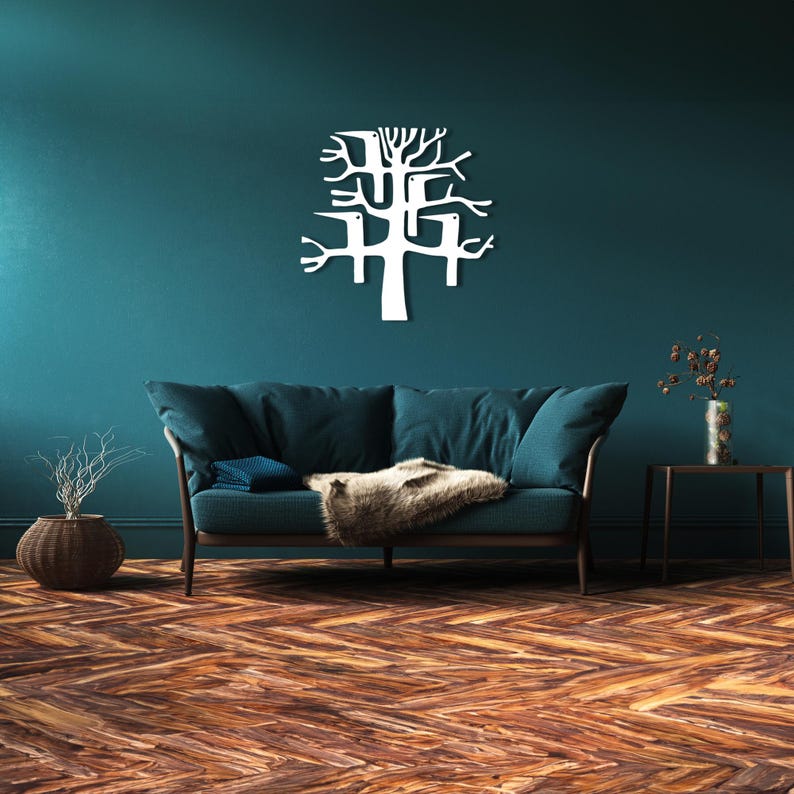 May include: A white metal tree wall art decor is mounted on a teal wall above a teal sofa with a brown wooden frame. The room has a wooden floor with a herringbone pattern. A decorative vase and side table are also visible.