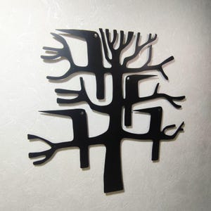 May include: Black metal wall art depicting a stylized tree with birds. The artwork features a central trunk with branches and several bird silhouettes integrated into the design. The piece is mounted on a textured, off-white wall.