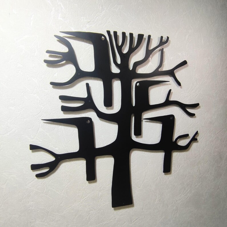 May include: Black metal wall art depicting a stylized tree with birds. The artwork features a central trunk with branches and several bird silhouettes integrated into the design. The piece is mounted on a textured, off-white wall.
