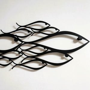 May include: Black metal wall art featuring a school of stylized fish. The fish are depicted with flowing lines and simple shapes, creating a modern and minimalist aesthetic. The artwork is mounted on a white background.
