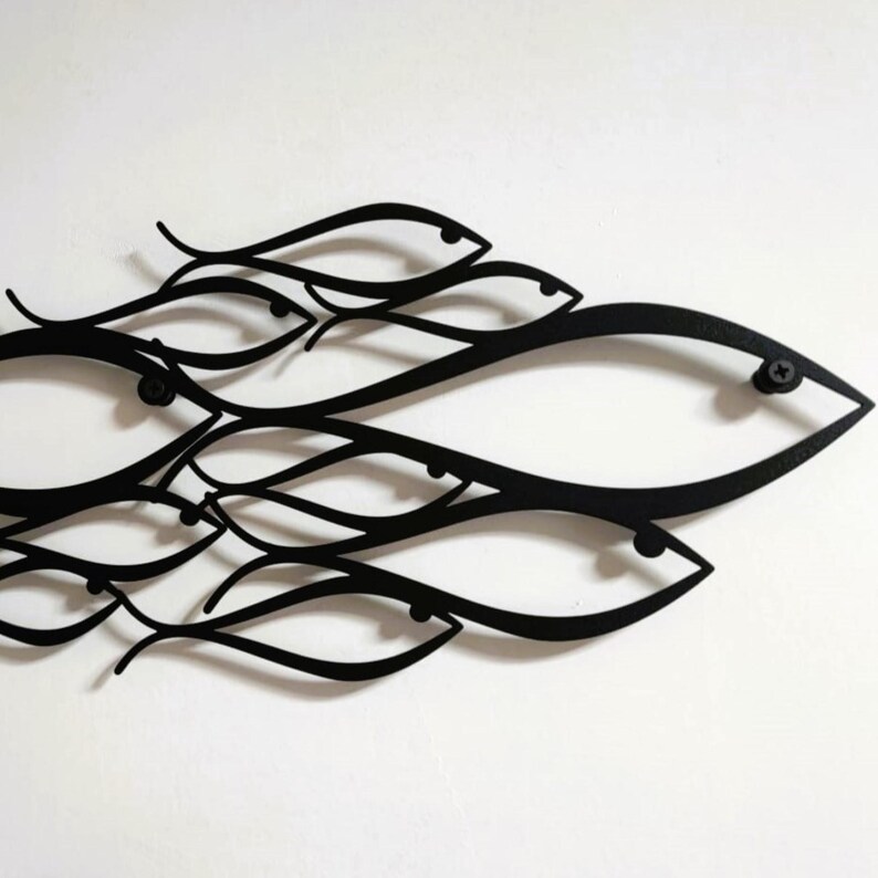 May include: Black metal wall art featuring a school of stylized fish. The fish are depicted with flowing lines and simple shapes, creating a modern and minimalist aesthetic. The artwork is mounted on a white background.