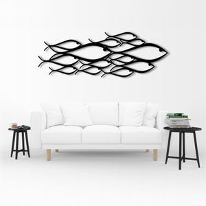 May include: A black metal wall art piece depicting a school of fish. The fish are stylized with curved lines and eye details. The artwork is mounted on a white wall above a white sofa. The room also includes two black side tables.