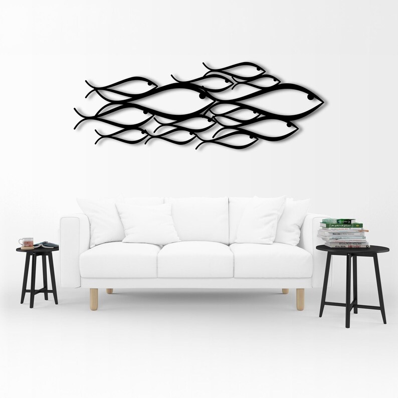 May include: A black metal wall art piece depicting a school of fish. The fish are stylized with curved lines and eye details. The artwork is mounted on a white wall above a white sofa. The room also includes two black side tables.