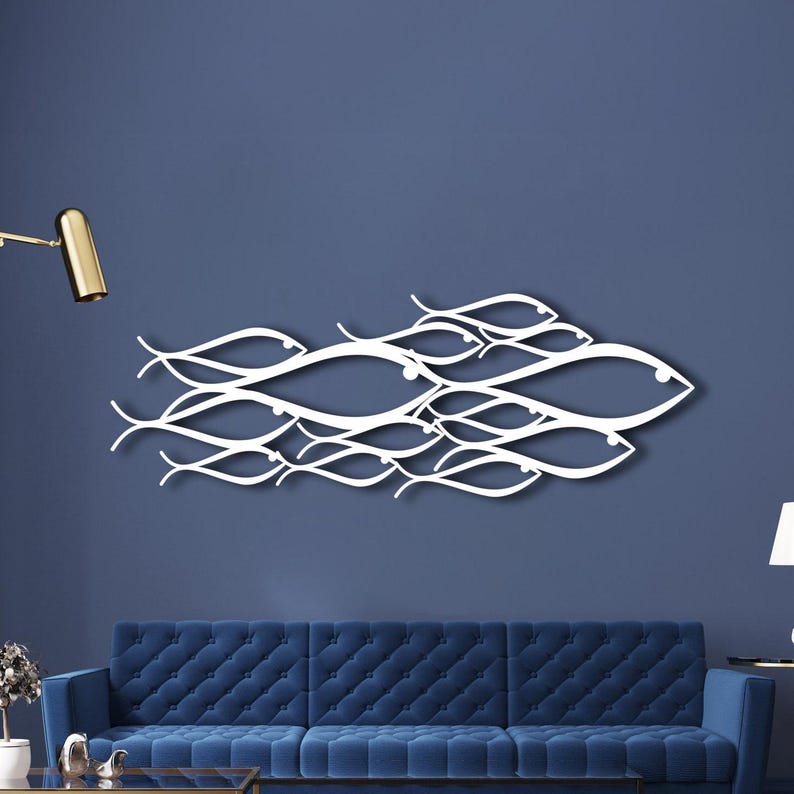 May include: White metal wall art depicting a school of fish. The artwork is composed of interconnected, stylized fish shapes, creating a flowing, aquatic design. The piece is mounted on a dark blue wall, above a blue sofa.