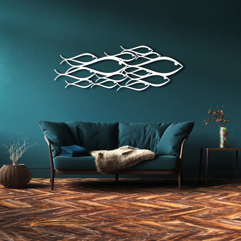 May include: A white metal wall art piece depicting a school of fish swimming together. The artwork is mounted on a teal wall above a blue sofa with a brown wooden frame. The room has a hardwood floor.