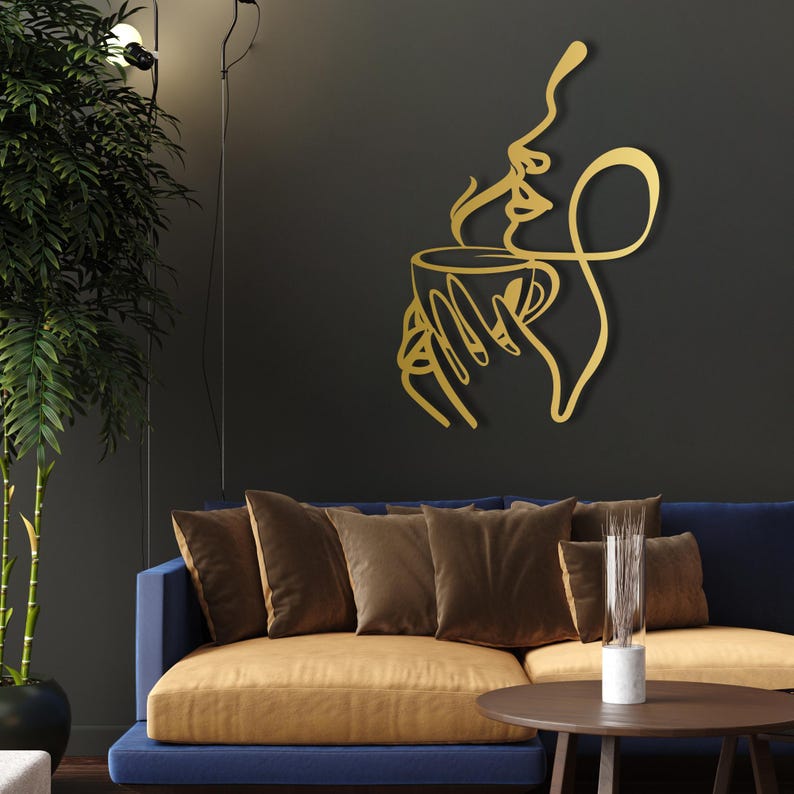 K&ouml;nnte beinhalten: Goldene Wandkunst aus Metall, die eine stilisierte Person darstellt, die eine Tasse Kaffee mit aufsteigendem Dampf h&auml;lt.