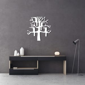 May include: A white metal tree wall art piece with a modern design is mounted on a dark gray wall. The tree has a stylized, abstract form with branches and a trunk. A black and wood-tone console table with decorative vases and a lamp is below.