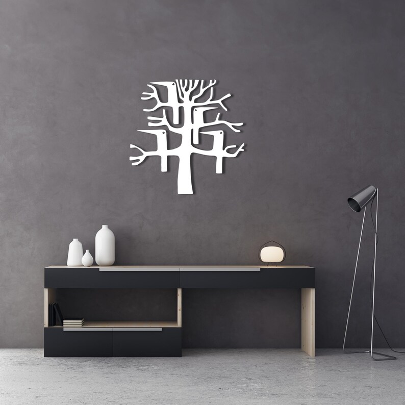 May include: A white metal tree wall art piece with a modern design is mounted on a dark gray wall. The tree has a stylized, abstract form with branches and a trunk. A black and wood-tone console table with decorative vases and a lamp is below.