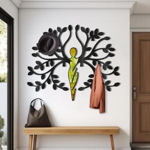 May include: Black metal wall-mounted coat rack shaped like a tree with a stylized human figure in the center. The rack has multiple hooks for hanging coats, hats, and bags.