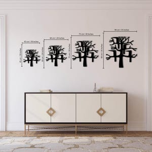 May include: Four black metal tree wall art pieces of varying sizes are displayed against a white wall. The sizes are 18 inches, 24 inches, 30 inches, and 35 inches. The art is above a white cabinet with gold accents.