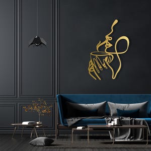 K&ouml;nnte beinhalten: Goldene Wandkunst aus Metall, die eine stilisierte Frau darstellt, die eine Tasse Kaffee mit aufsteigendem Dampf h&auml;lt. Die Kunst ist an einer schwarzen Wand in einem modernen Wohnzimmer angebracht.