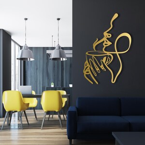 K&ouml;nnte beinhalten: Goldene Wandkunst aus Metall, die eine stilisierte Linienzeichnung einer Person darstellt, die eine dampfende Tasse Kaffee h&auml;lt. Die Kunst ist an einer dunkelgrauen Wand in einem modernen Wohnzimmer angebracht.