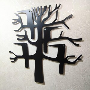 May include: Black metal wall art depicting a stylized tree with birds. The artwork features a minimalist design with cut-out shapes of branches and birds, creating a modern and artistic aesthetic. The piece is mounted on a textured, off-white wall.