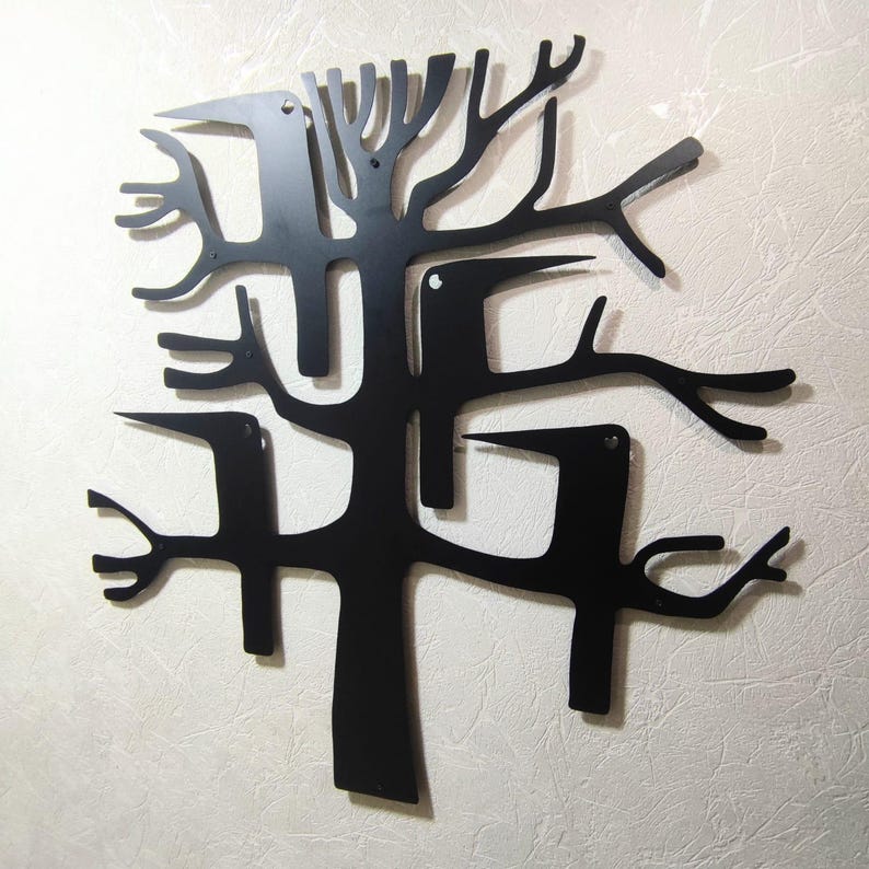 May include: Black metal wall art depicting a stylized tree with birds. The artwork features a minimalist design with cut-out shapes of branches and birds, creating a modern and artistic aesthetic. The piece is mounted on a textured, off-white wall.