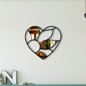 May include: A black metal heart-shaped wall mirror with a geometric design. The mirror reflects a room with a door and a window.