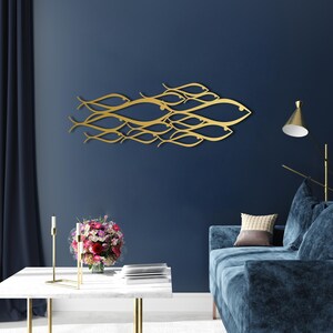 May include: A gold-colored metal wall art piece depicting a school of fish swimming together. The artwork is mounted on a dark blue wall, creating a striking contrast. The fish are stylized with flowing lines.