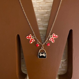 May include: Gold chain necklace with red and white polka dot bows, red hearts, and a black purse charm with a rhinestone bow.