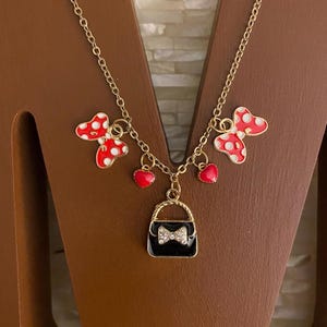 May include: Gold chain necklace with red and white polka dot bows, red heart charms, and a black purse charm with a rhinestone bow.