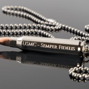 May include: A silver bullet necklace with a chain and the inscription "USMC - SEMPER FIDELIS".