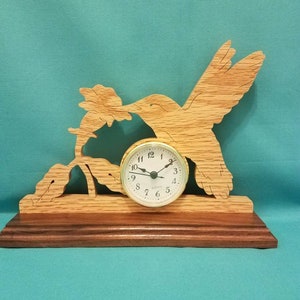 May include: A wooden clock featuring a hummingbird in flight, with a flower in its beak. The clock is mounted on a wooden base.