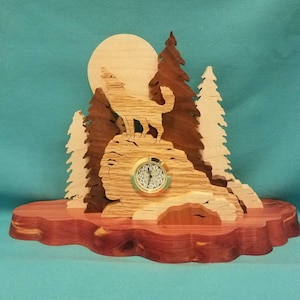 May include: Wooden clock with a wolf howling at the moon, surrounded by trees. The clock is on a wooden base.