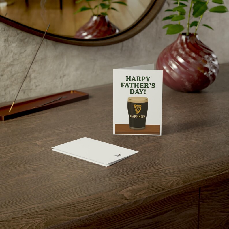 May include: A Father's Day card with the text "HARPY FATHER'S DAY!" and an illustration of a pint of stout. The card is on a wooden surface with a blank envelope in front. A decorative vase and incense burner are in the background.