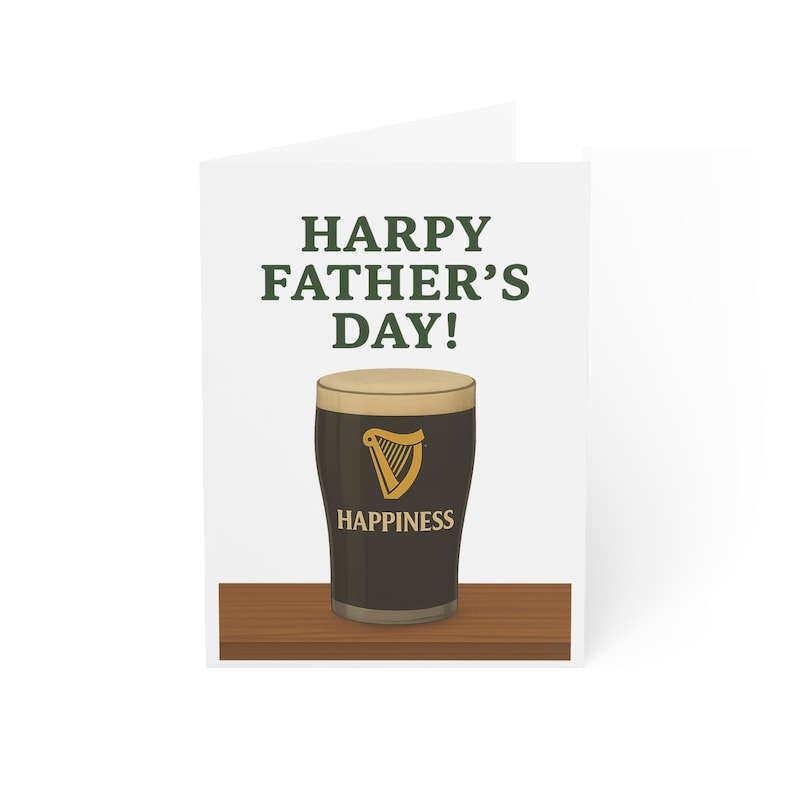 May include: A white Father's Day greeting card with the text "HARPY FATHER'S DAY!". The card features a pint of dark stout with a creamy head, a gold harp logo, and the word "HAPPINESS" below the glass. The card is on a wooden surface.