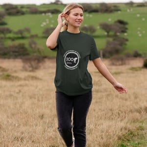 Op de afbeelding: Een donkergroen T-shirt met een witte cirkelvormige afbeelding met de tekst "One foot in front of the other 100 without passing out".