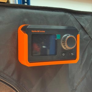Könnte beinhalten: Ein schwarzer digitaler Spider Farmer Controller in einer leuchtend orangefarbenen Kunststoffhalterung. Das Gerät verfügt über einen rechteckigen Bildschirm, einen runden Einstellknopf mit orangefarbenem Rand und zwei kleine Tasten.