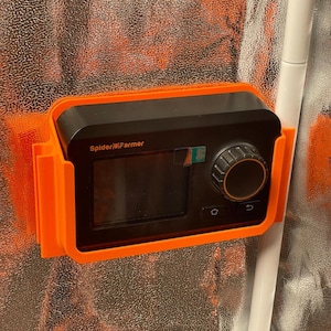 Könnte beinhalten: Ein schwarzer und orangefarbener Spider Farmer-Controller ist montiert. Das Gerät verfügt über ein digitales Display, einen Drehregler und Tasten. Der Markenname "Spider Farmer" ist auf dem Gerät aufgedruckt.