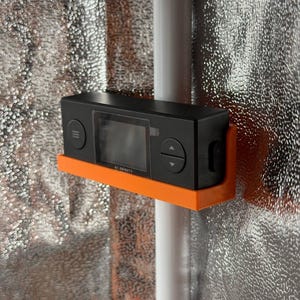 Könnte beinhalten: Ein schwarzer digitaler AC Infinity-Controller in einer orangefarbenen Kunststoffhalterung an einer vertikalen weißen Stange. Das rechteckige Gerät verfügt über einen zentralen Bildschirm, eine Menütaste links und Pfeiltasten rechts.