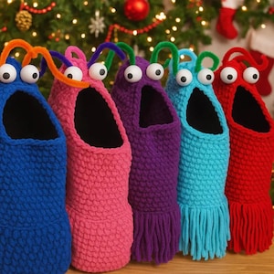 Può includere: Una fila di pantofole colorate a tema mostro in blu, rosa, viola, turchese e rosso. Ogni pantofola ha grandi occhi mobili e antenne in scovolini. Le pantofole hanno un design a maglia strutturata e un fondo con frange.