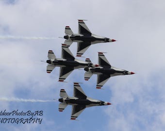 Puede incluir: Cuatro aviones de combate blancos y negros vuelan en formación contra un cielo azul con nubes blancas. Los aviones vuelan en formación de diamante con el avión líder en la parte superior.