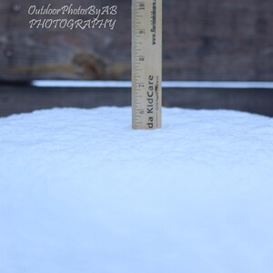 Op de afbeelding: Een houten liniaal van 30,5 cm lang staat rechtop in een bedje van verse, witte sneeuw. De liniaal is gemarkeerd met nummers en de tekst "da Kid Care Child Healthcare" is aan de zijkant gedrukt.