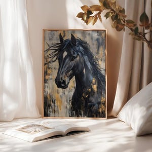 May include: A framed art print depicting a black horse with a flowing mane. The painting has a textured background with gold and neutral tones. The artwork is displayed on a white surface with an open book.