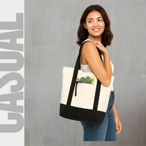 May include: A canvas tote bag with a black base and straps, and a cream-colored body. The bag has a front pocket with a black zipper and a green plant inside. The word "CASUAL" is printed in large gray letters on the left.