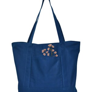 May include: A navy blue tote bag with a floral design. The bag has two long straps and a front pocket. The floral design features light orange flowers with green stems. The bag is made of a sturdy material.