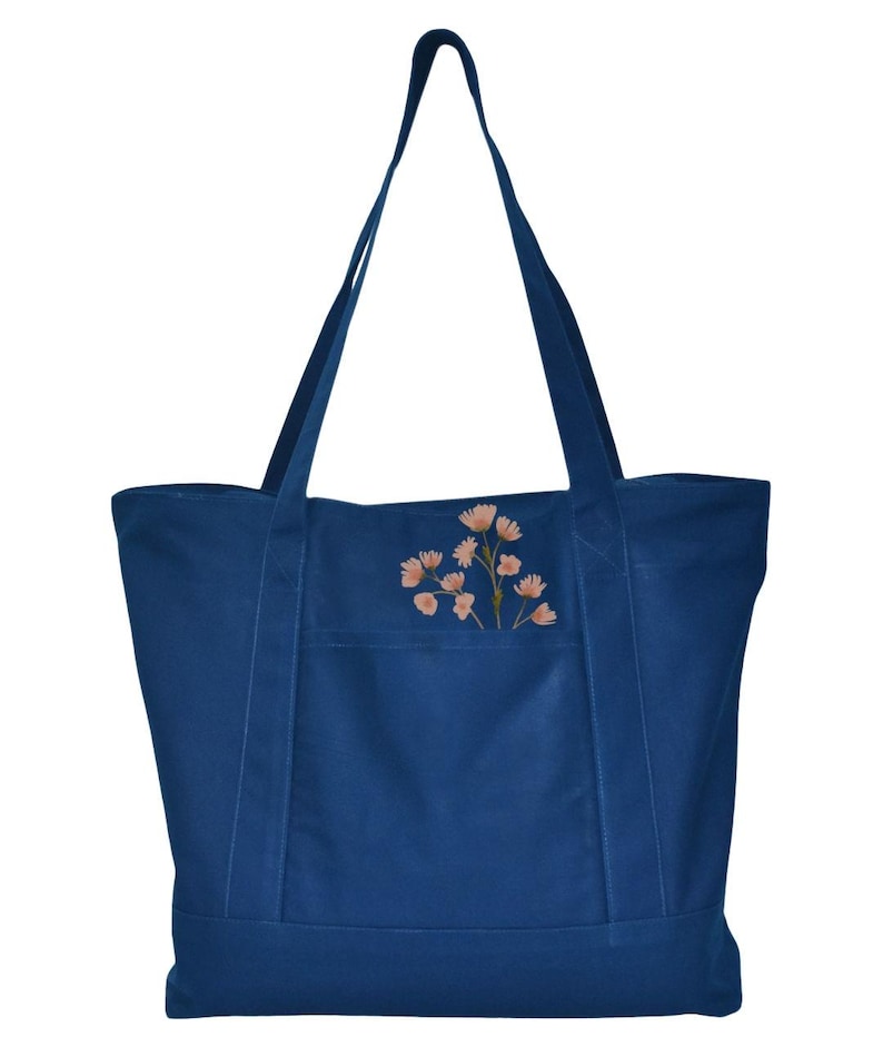 May include: A navy blue tote bag with a floral design. The bag has two long straps and a front pocket. The floral design features light orange flowers with green stems. The bag is made of a sturdy material.