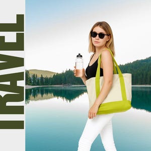 May include: A woman wearing sunglasses, a black tank top, and white pants, carries a water bottle and a cream-colored tote bag with green accents. The word "TRAVEL" is printed vertically in large, dark green letters.