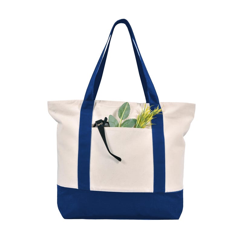 May include: A canvas tote bag with a cream-colored body and a navy blue base and straps. The bag has a front pocket and is filled with greenery. The tote bag is designed for carrying items.